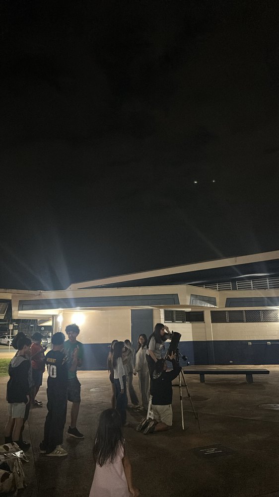 Students gathered around a telescope at night, looking up at the stars