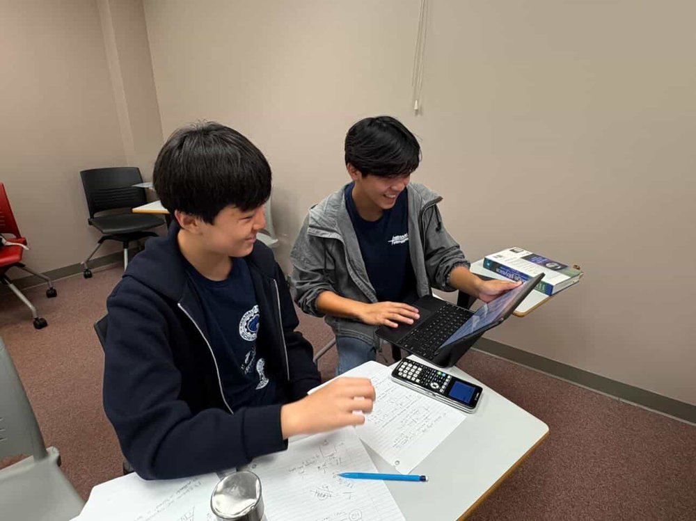 Two students working together on a Science Olympiad problem with a laptop and calculator