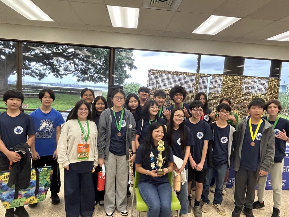 A high school STEM team celebrating with medals and a trophy at a competition